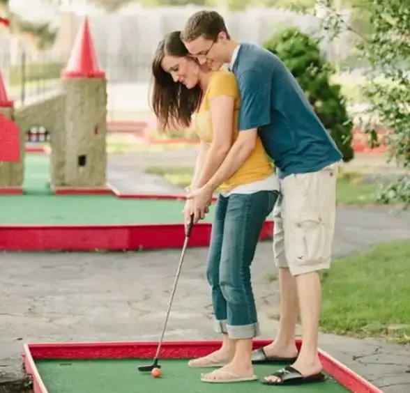 woman and man at the back helping her aim a goal at a mini golf