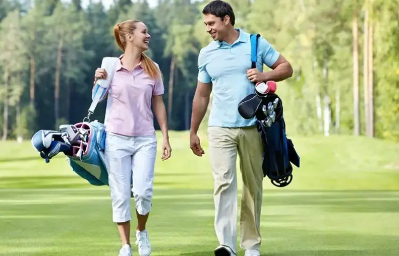 a woman and man carrying their golf bag with accessories walking at the golf course smiling to each other